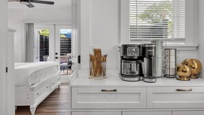 A bedroom with a bed, a ceiling fan, a coffee maker, and a window with blinds. - La Barra #101 (St. Pete Beach)
