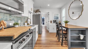 A modern kitchen with white cabinets, a wooden countertop, and a stainless steel range hood. - La Barra #101 (St. Pete Beach)