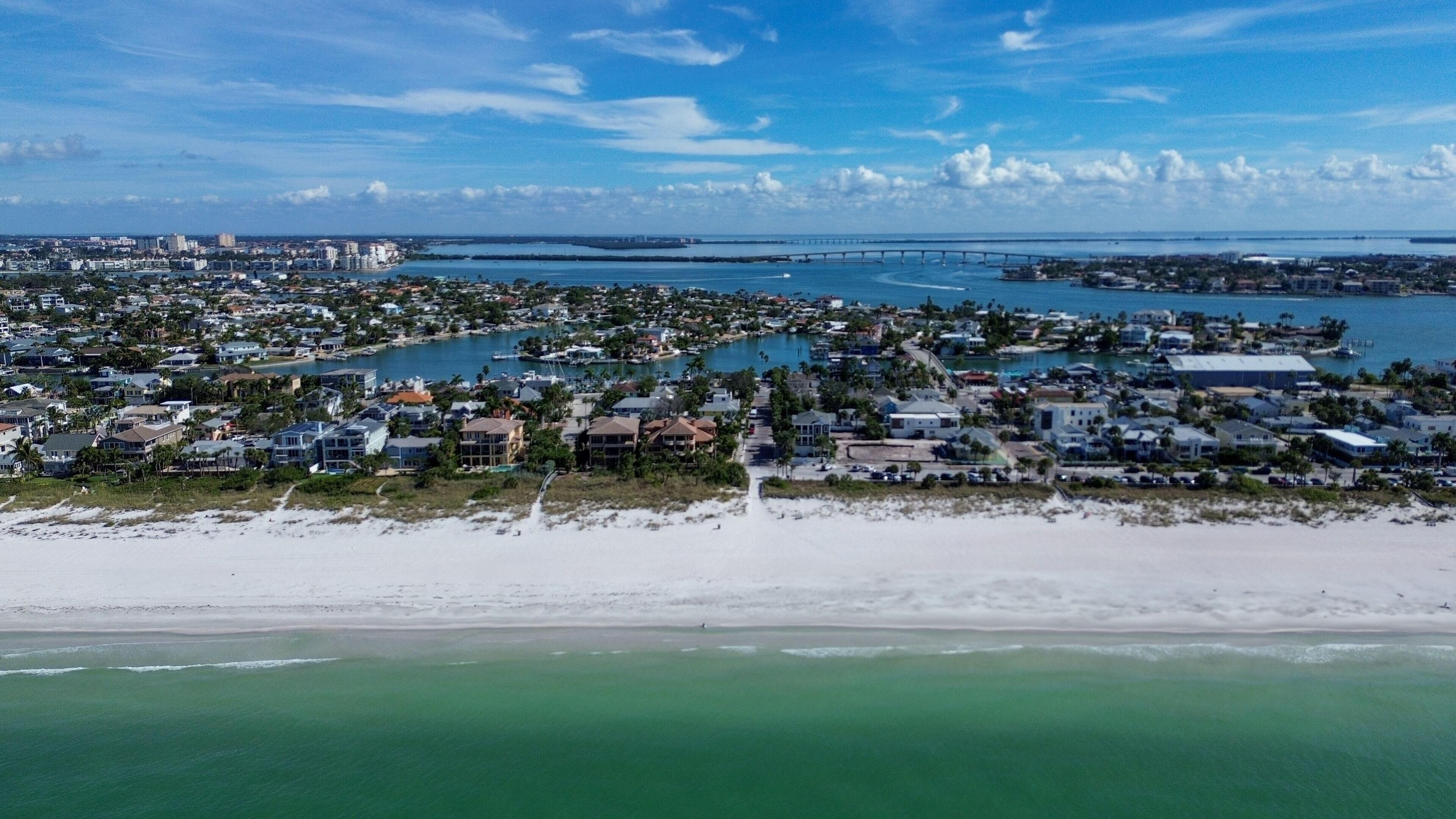 A coastal town with residential buildings, a beach, and a bridge in the distance.