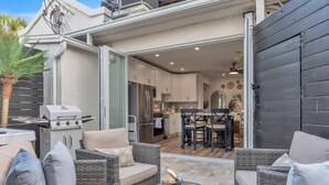 Een terras buiten met rieten meubilair, een barbecue en een eethoek met tafel en stoelen.