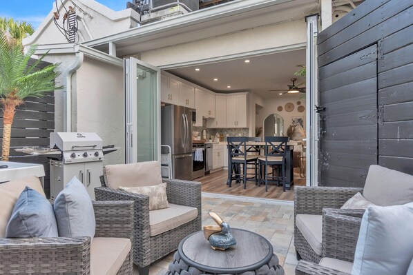 Une terrasse extérieure aménagée avec des meubles en osier, un barbecue et un coin repas comprenant une table et des chaises.