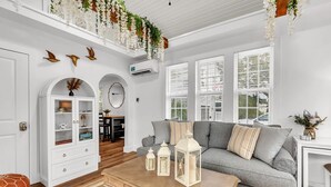 Een woonkamer met een grijze bank, een wit kastje en hangende planten.