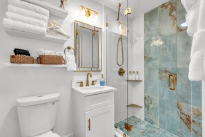 Une salle de bain moderne équipée de toilettes, d’un lavabo et d’une douche. Des serviettes et des articles de toilette sont disposés sur des étagères.