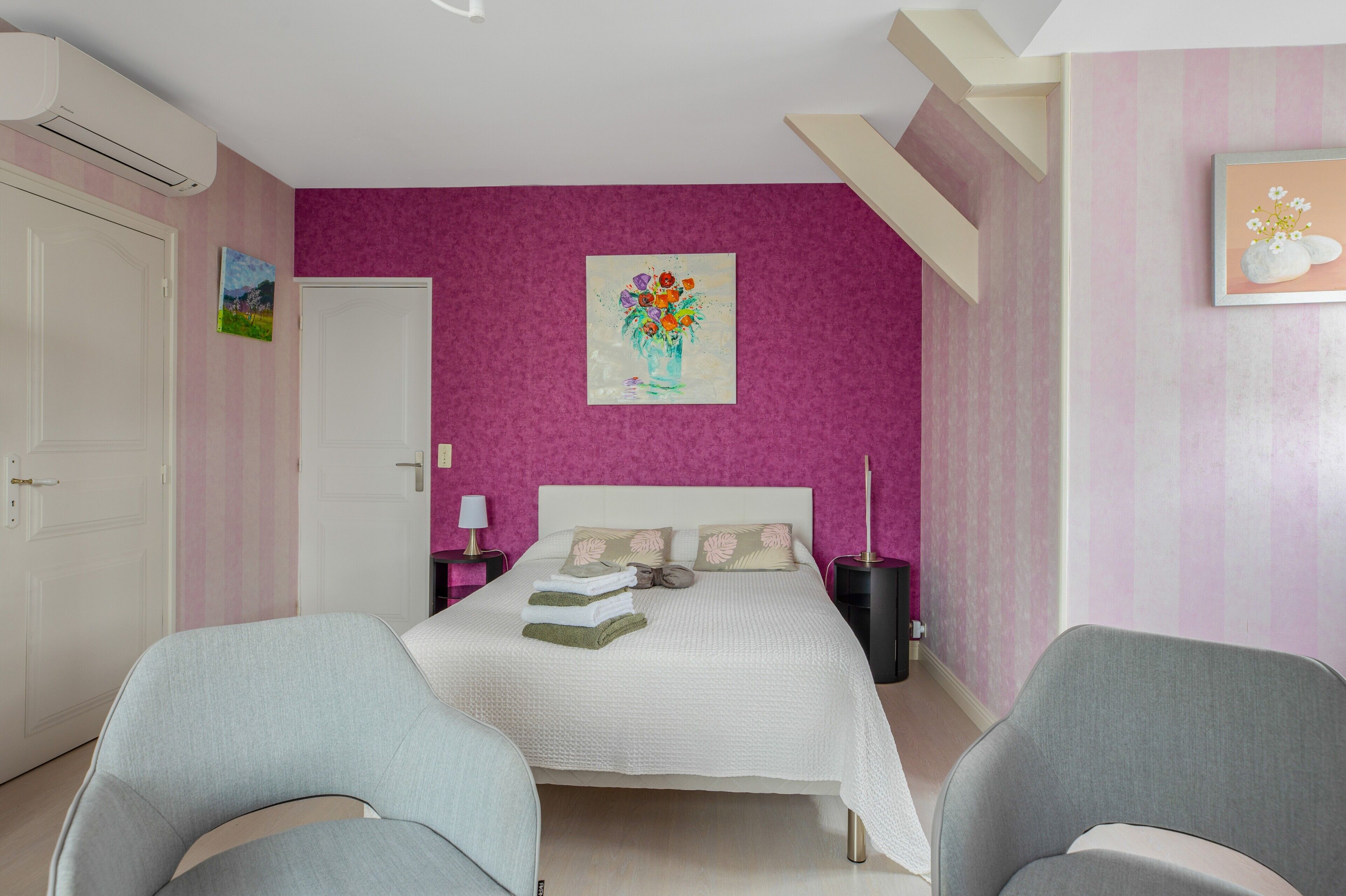 Een slaapkamer met een bed, twee stoelen, een schilderij en een deur.
