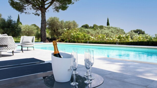 Une scène au bord de la piscine, avec une bouteille de champagne, des verres et une table.