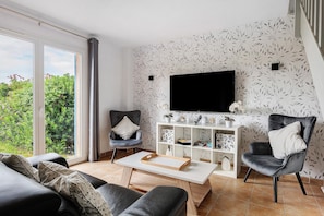 A modern living room with a sofa, armchairs, a coffee table, and a TV on a wall with leaf-pattern wallpaper.