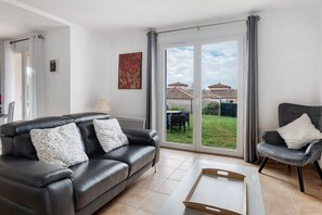 A living room with a leather sofa, a dining table, and a sliding glass door leading to a patio. - Les Villas du Port Minervois - A6 (Homps)