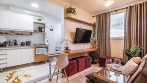 Un apartamento moderno con cocina, comedor y sala de estar. Cuenta con un televisor de pantalla plana, un sofá y una mesa de comedor con dos copas de vino.
