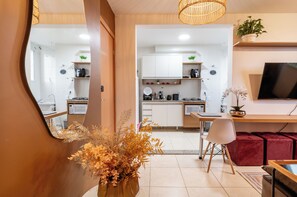 Una cocina moderna con armarios blancos, una zona de comedor con un pouf rojo y un televisor montado en la pared.