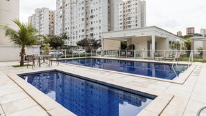 Una piscina con sillas de descanso y una zona cubierta, rodeada de edificios residenciales altos.
