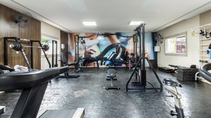Un gimnasio con diversos equipos de ejercicio, un mural en la pared y una ventana con vistas al exterior.