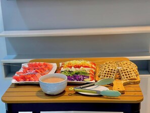 A wooden table with a variety of food items including sliced watermelon, a colorful salad, waffles, and a bowl of soup. - Iri Diplomatic Resorts (Abuja)