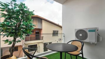 Un balcon avec un revêtement de gazon synthétique, deux fauteuils en osier, une plante en pot et un climatiseur fixé au mur.