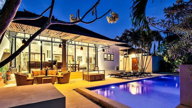 Una casa moderna con piscina, zona de estar exterior y un patio cubierto de cristal.
