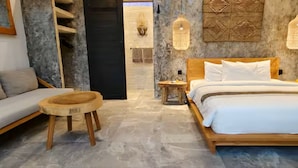 Un dormitorio moderno con una cama de madera, un sofá gris y un taburete redondo de madera.