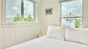 A bedroom with two large windows, a bed with white bedding, and a framed picture on the wall. - Private Downtown Bar Harbor Four-Apartment Home (Bar Harbor)