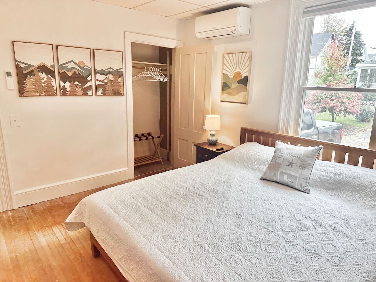 Een slaapkamer met een bed, nachtkastje, lamp, raam met uitzicht en een inloopkast met kledingroede.