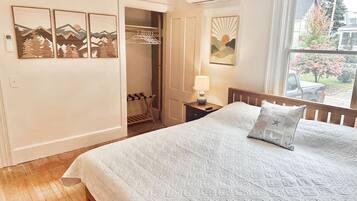 Een slaapkamer met een bed, nachtkastje, lamp, raam met uitzicht en een inloopkast met kledingroede.