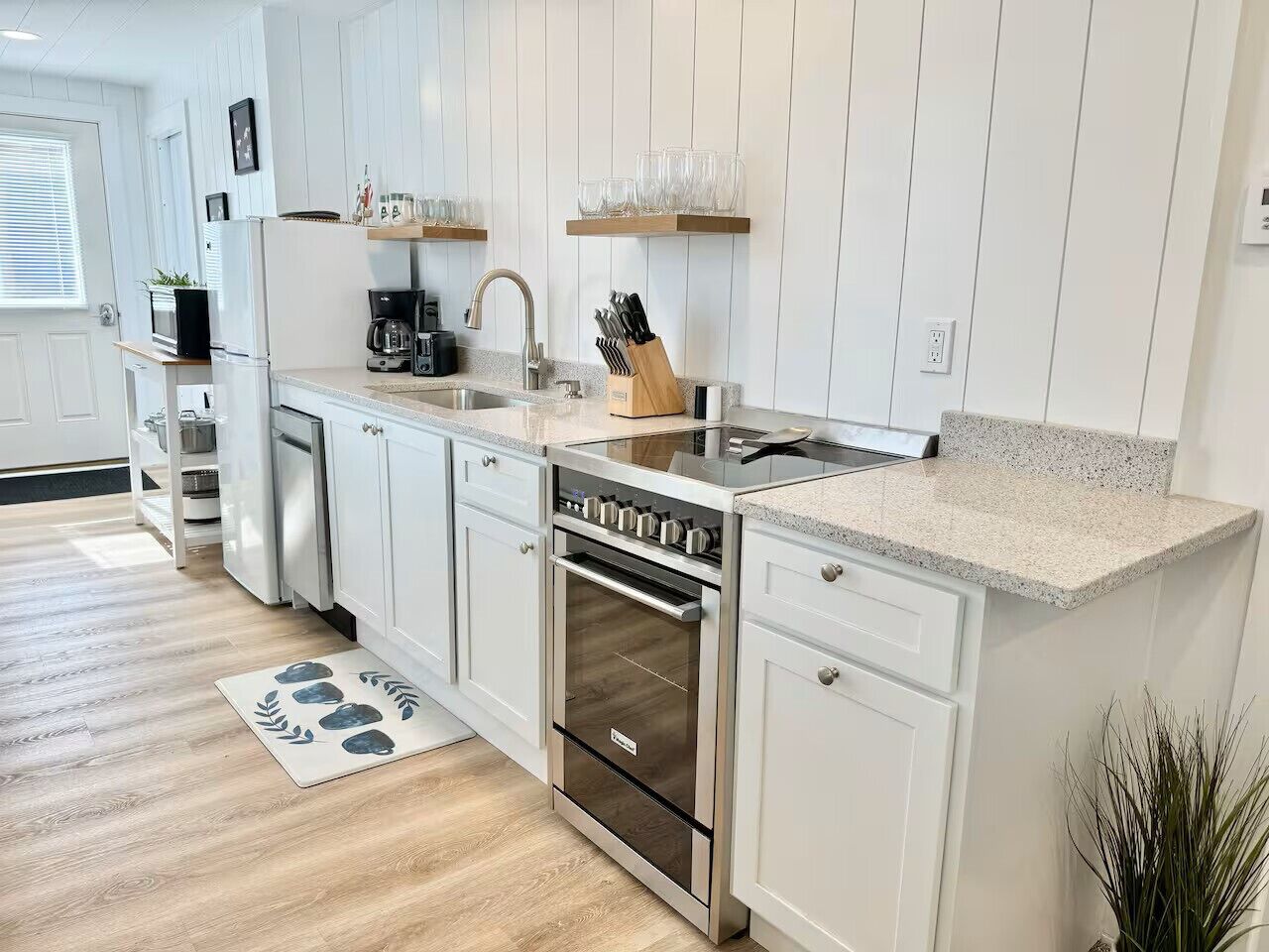 A modern kitchen with white cabinetry, a stainless steel oven, a built-in dishwasher, and a granite countertop.