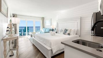 A hotel room with a bed, a desk, a sink, and a balcony with a view of the sea.