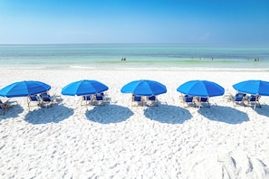 A beach with five blue umbrellas and beach chairs aligned in a row.