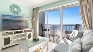 A living room with a television, a glass coffee table, a sofa, and a view of the ocean through large sliding glass doors. - Gorgeous Studio with Free Beach Service for 2 at Islander Beach Resort 504 (Fort Walton Beach)