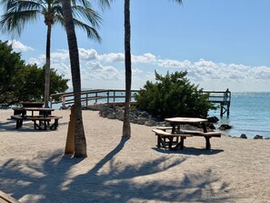 A beach with picnic tables, palm trees, and a wooden pier extending into the water. - Key Colony Beach Home Casa Sunny Sea Key Colony Beach, Fl Keys (Key Colony Beach)