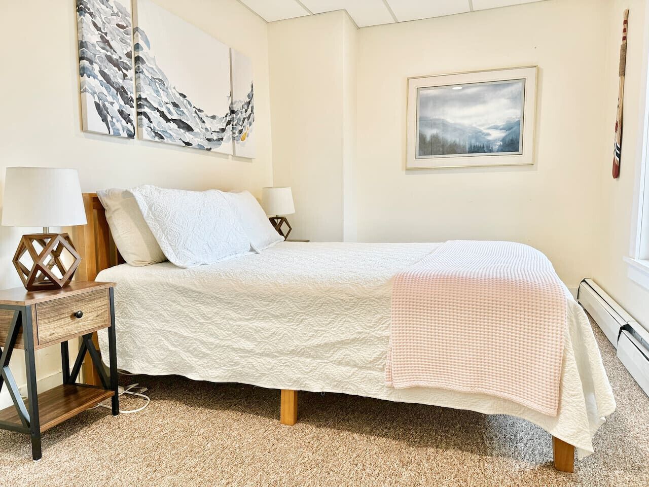 A bedroom with a bed, bedside tables, lamps, and artwork on the walls.