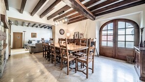 A spacious dining area with a wooden table and chairs, a clock on the wall, and a large arched window.