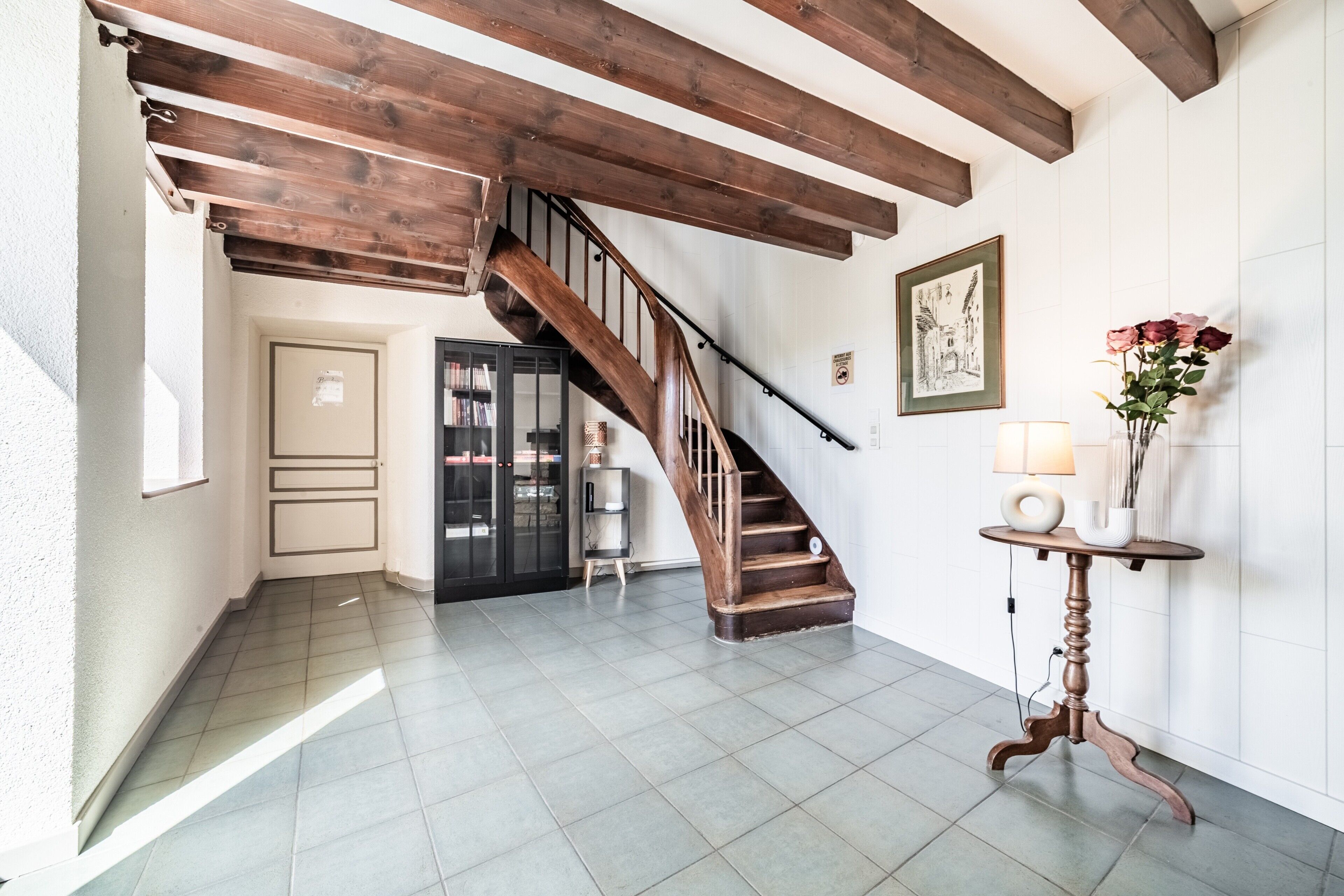 Eine Treppe mit hölzernen Geländern, ein kleiner Tisch mit einem Blumenstrauß und ein gerahmtes Bild an der Wand.