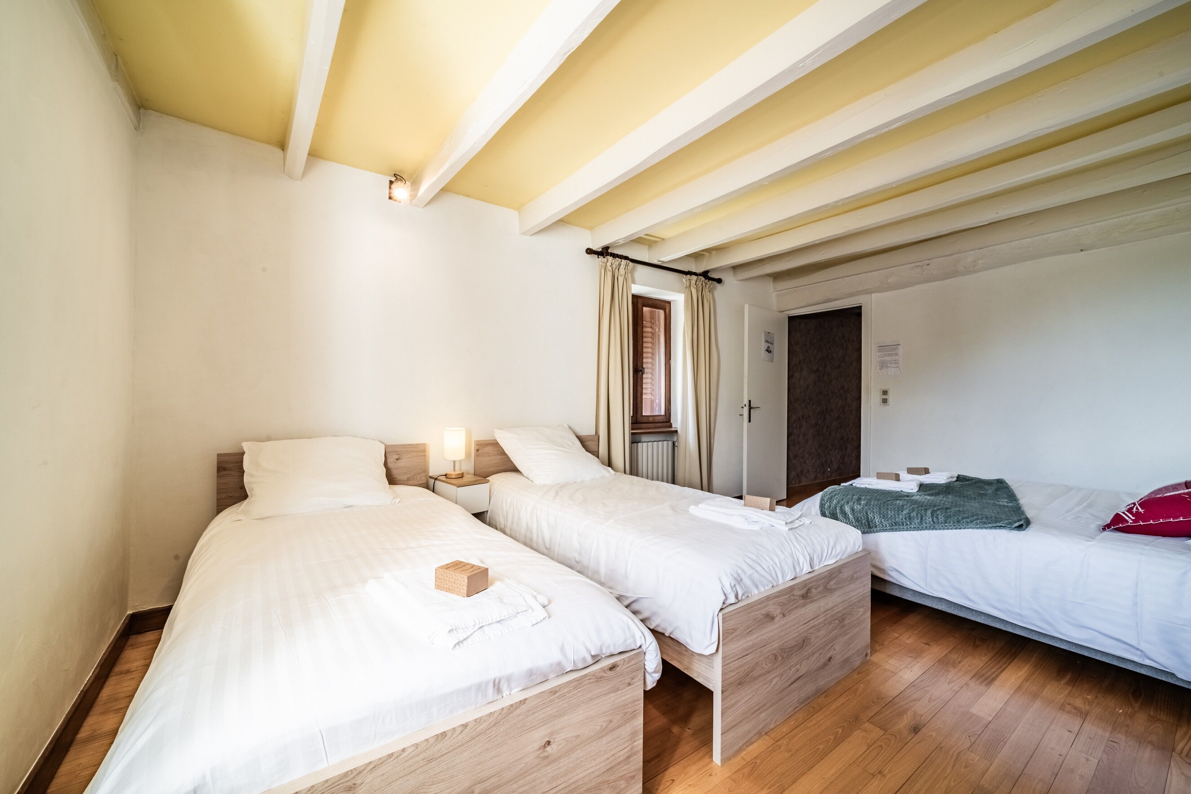 A room with two wooden beds, a wooden floor, and a white ceiling with exposed beams.
