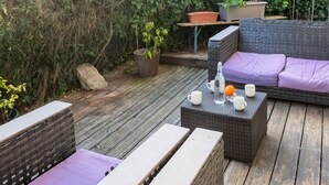Un patio al aire libre con mobiliario de mimbre, una mesa con tazas y una botella, y una planta en maceta.