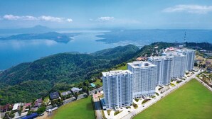 A high-rise hotel complex with multiple floors, surrounded by lush greenery and a view of a large body of water. - WIND TAAL TAGAYTAY PHILIPPINES (Tagaytay City)