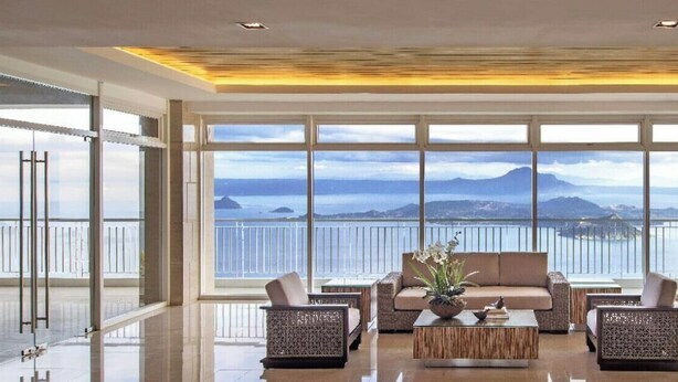 A spacious living room with a large window offering a view of the sea and mountains. There are two sofas and two armchairs arranged around a coffee table. - WIND TAAL TAGAYTAY PHILIPPINES (Tagaytay City)