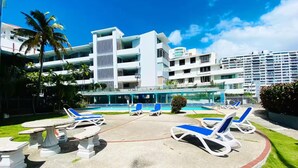 Ett semesterhotell med poolområde, solstolar och en modern byggnad med balkonger.