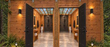 A wooden cabin with two doors, a shower area, and a small garden with stepping stones and lights.