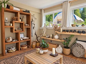 A cozy room with a wooden bookshelf, a table with candles, and a window with a view of greenery.