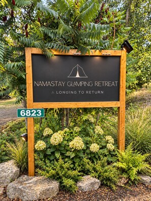 A sign for a camping retreat with a tent logo, surrounded by greenery and rocks.