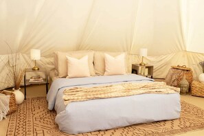 A tent-style room with a bed, pillows, a lamp, a bedside table, and a woven basket.