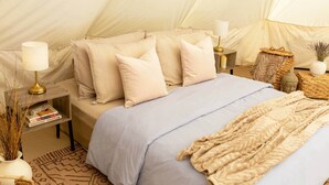 A tent-style room with a bed, pillows, a lamp, a bedside table with books, and decorative items.