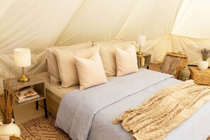 A tent-style room with a bed, pillows, a lamp, a bedside table with books, and decorative items.
