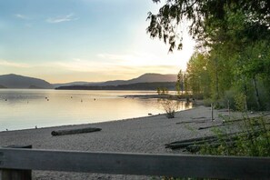 A beach with calm water, a wooden fence, and trees.