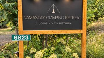 A sign for a camping retreat with a tent logo, surrounded by greenery and rocks.