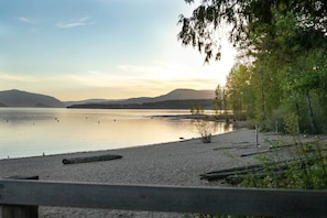 A beach with calm water, a wooden fence, and trees.