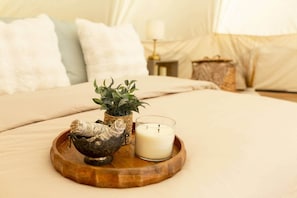 A bed with a white comforter, a wooden tray with a candle, a small plant, and a decorative bowl.