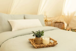 A bed with a light-colored duvet, a small woven basket with a candle and a plant, and a white pillow.