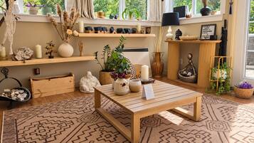 Une pièce avec une table en bois, un tapis à motifs et divers objets décoratifs, notamment une statue de Bouddha, des bougies et des plantes.