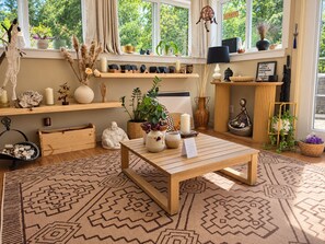 Une pièce avec une table en bois, un tapis à motifs et divers objets décoratifs, notamment une statue de Bouddha, des bougies et des plantes.