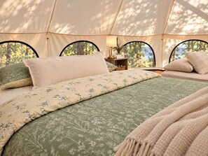 A tent with a bed, pillows, a lamp, and a view of trees. - Kula at Namastay Glamping Retreat (Columbia-Shuswap)