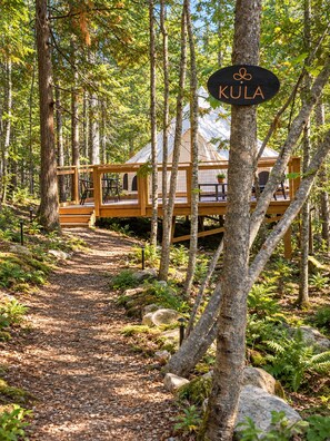 A forested area with a wooden deck leading to a tent-like structure labeled 'KULA'. - Kula at Namastay Glamping Retreat (Columbia-Shuswap)